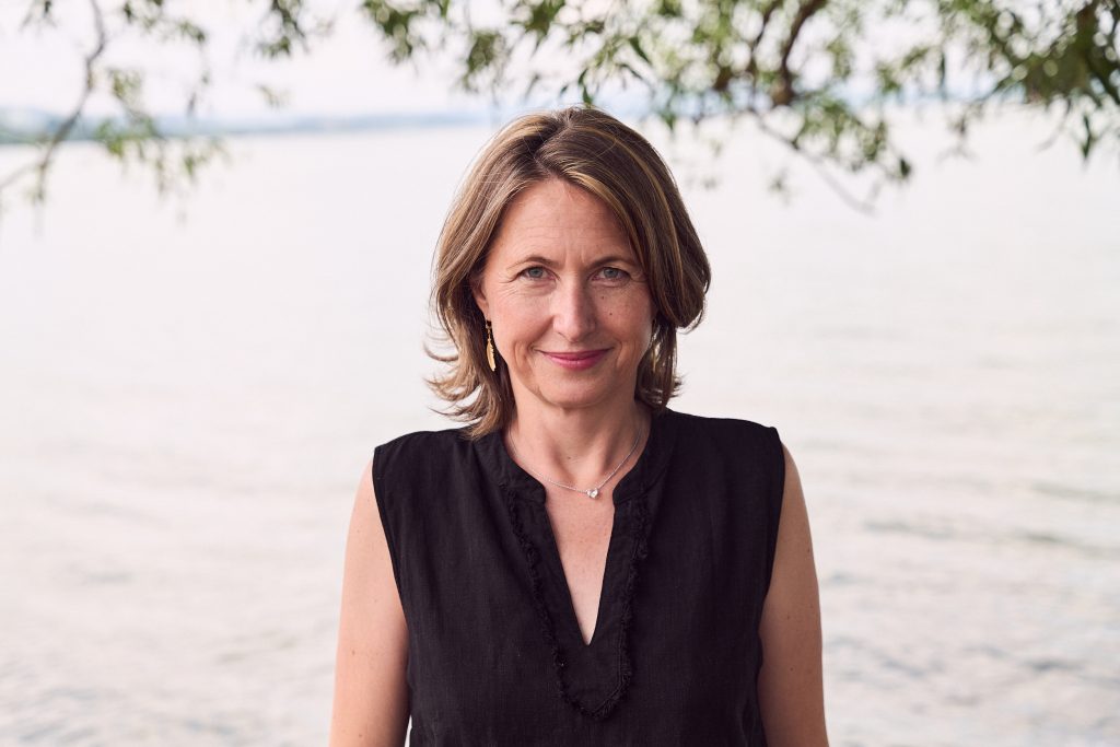 Priska Portmann steht am Seeufer, ruhiger Blick in die Kamera