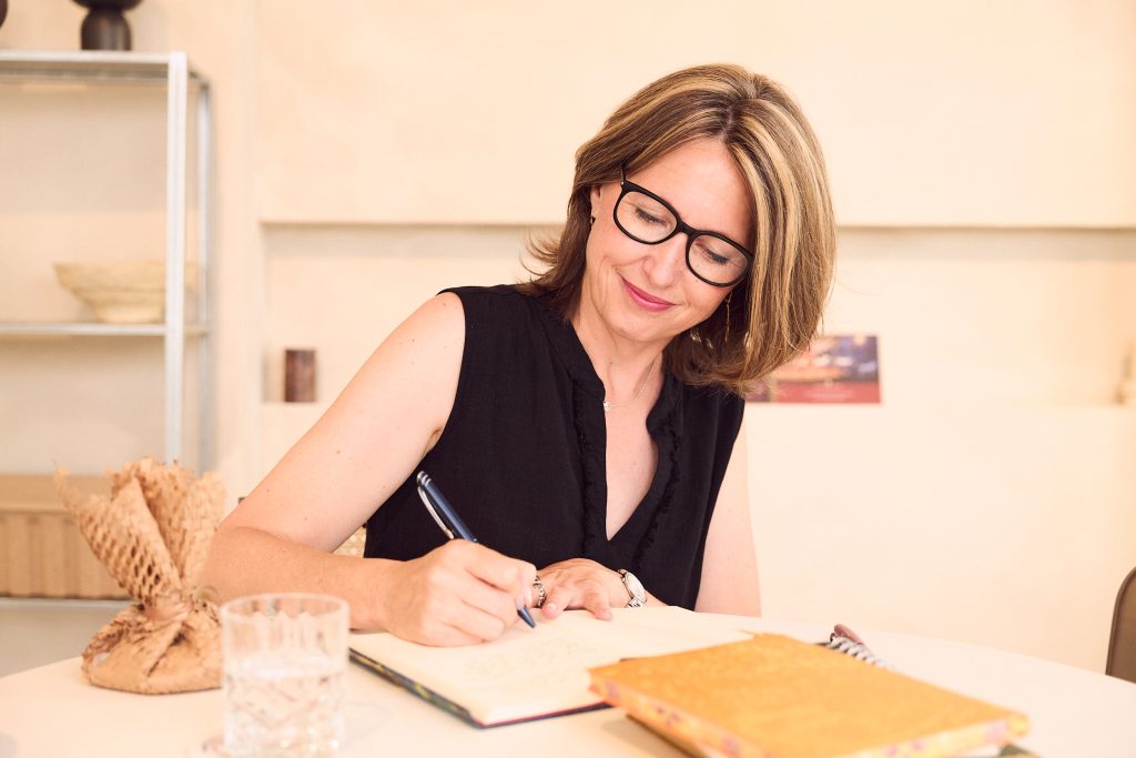 Priska sitzt am Tisch und schreibt in ihr Notizbuch für den Blog